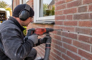 Boorgaten maken in de gevel voor het aanbrengen van spouwmuurisolatie Isolatiespecialist boort gaten in de voegen van een bakstenen gevel ter voorbereiding op spouwmuurisolatie